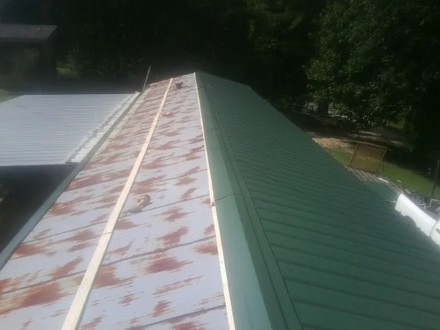 Old rusted panels beside newly installed green metal roofing — Wind Damage Roof Repair by Roofing Brothers in Salina