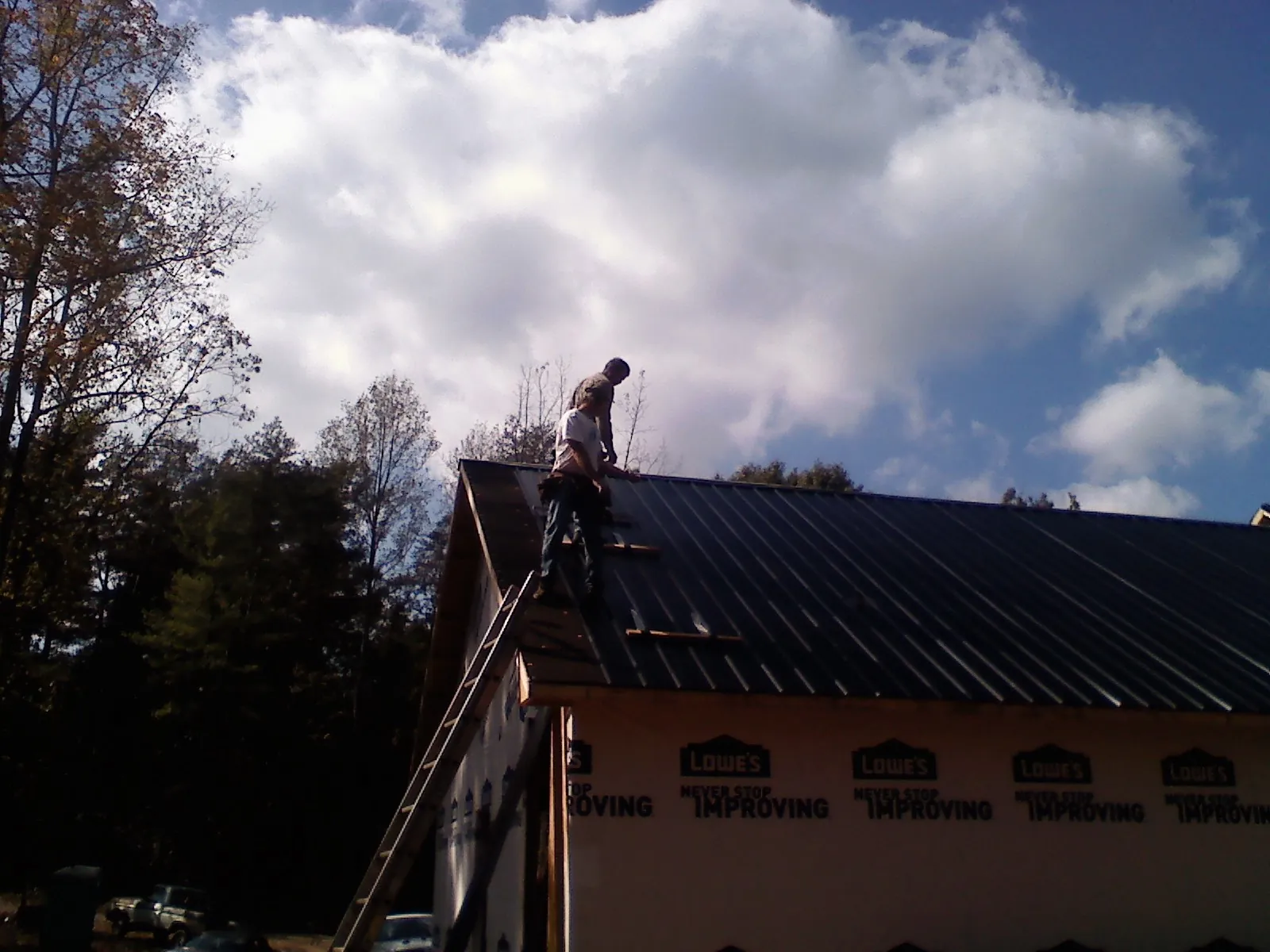 Roofer fastening dark metal panels high against a cloudy sky, from a Roof Inspection job in Salina